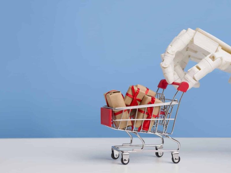 robot-hand-with-shopping-cart-full-of-gift-boxes-blue-background.jpg